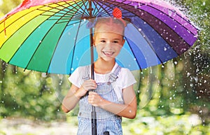 Happy child girl laughs and plays under summer rain with an umbrella.