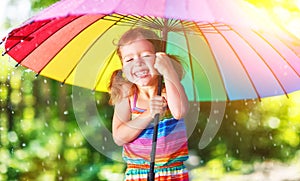 Happy child girl laughs and plays under summer rain with an umbrella