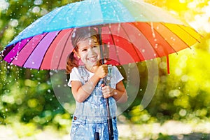 Happy child girl laughs and plays under summer rain with an umbrella.