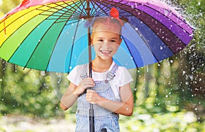 Happy child girl laughs and plays under summer rain with an umbrella. photo