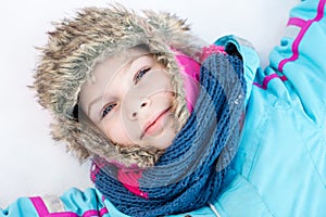 Happy child girl laying down on a frozen clear snow