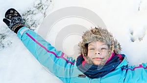 Happy child girl laying down on a frozen clear snow