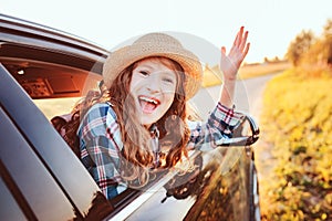 Happy child girl looking out the car window during road trip on summer vacations.