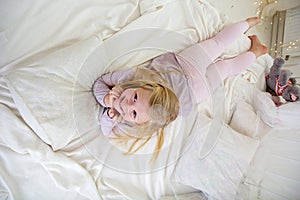 Happy child girl is lying down in the white bed