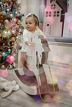 Happy child a girl of ont year old sits on a wooden horse against a new year Christmas tree photo