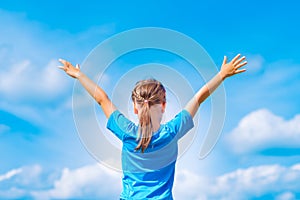 Happy child girl with open arms outdoor under blue sky. Young gi