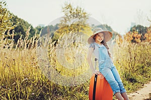 Happy child girl with orange suitcase traveling alone on summer vacation. Kid going to summer camp.