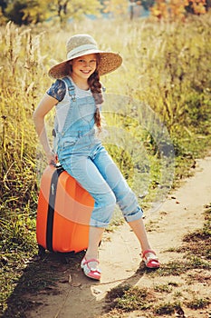 Happy child girl with orange suitcase traveling alone on summer vacation. Kid going to summer camp.