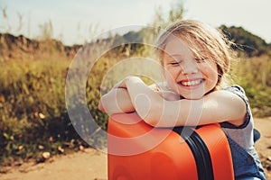 Happy child girl with orange suitcase traveling alone on summer vacation. Kid going to summer camp.