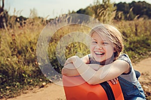 Happy child girl with orange suitcase traveling alone on summer vacation. Kid going to summer camp.