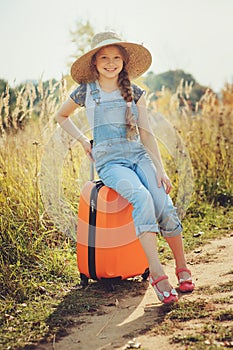 Happy child girl with orange suitcase traveling alone on summer vacation. Kid going to summer camp.