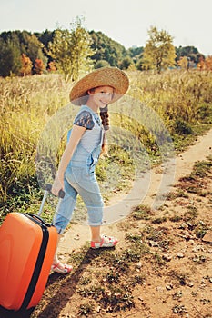 Happy child girl with orange suitcase traveling alone on summer vacation. Kid going to summer camp.