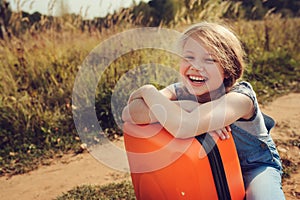 Happy child girl with orange suitcase traveling alone on summer vacation. Kid going to summer camp.