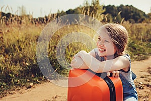 Happy child girl with orange suitcase traveling alone on summer vacation. Kid going to summer camp.