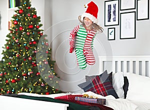 Happy child in pajamas with gifts jumping in bed on christmas m