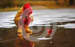 Happy child girl with paper boat in puddle in autumn on nature