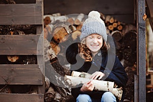 Happy child girl picking firewood from shed in winter