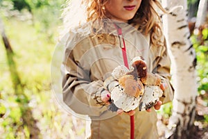 Happy child girl picking wild mushrooms on the walk in summer