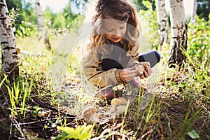 Happy child girl picking wild mushrooms on the walk in summer