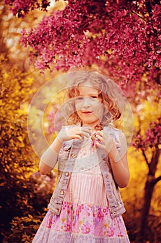 Happy child girl in pink dress playing outdoor in spring garden near blooming crabapple tree