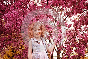 Happy child girl in pink dress playing outdoor in spring garden near blooming crabapple tree