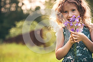 Happy child girl playing with bouquet of bluebells in summer.