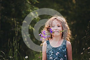 Happy child girl playing with bouquet of bluebells in summer.