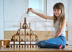 Happy child girl playing game stacking wooden toy blocks in high pile structure. Hand movement control and building