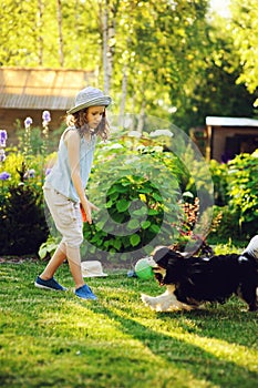 Happy child girl playing with her spaniel dog and throwing ball