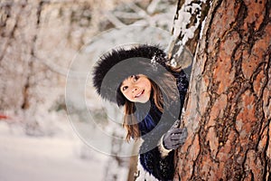 Happy child girl playing hide and seek in winter forest