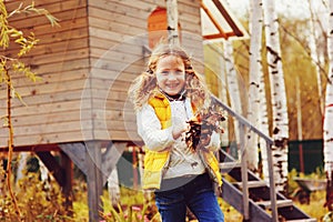 Happy child girl playing little gardener in autumn and picking leaves into basket