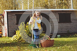 Happy child girl playing little gardener in autumn and picking leaves into basket. Seasonal garden work