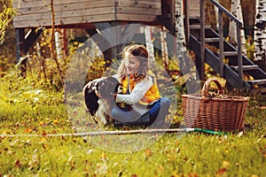 Happy child girl playing little gardener in autumn and picking leaves into basket. Seasonal garden work.