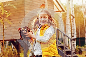 Happy child girl playing little gardener in autumn and picking leaves into basket. Seasonal garden work.