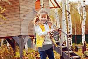 Happy child girl playing little gardener in autumn and picking leaves into basket. Seasonal garden work.