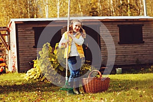 Happy child girl playing little gardener in autumn and picking leaves into basket. Seasonal garden work.