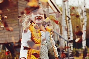 Happy child girl playing little gardener in autumn and picking leaves into basket. Seasonal garden work.