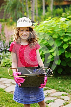 Happy child girl playing little gardener and helping in summer garden