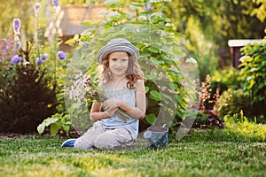 Happy child girl playing little gardener in summer, wearing funny hat and holding bouquet