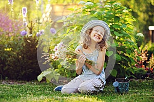 happy child girl playing little gardener in summer, wearing funny hat and holding bouquet of flowers