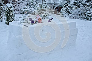 Happy child girl playing in snow castle in dropping snowballs on winter backyard