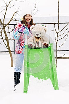 Happy child girl playing with teddy in the snow, winter time. Little toddler girl holding teddy bear, playing outdoors