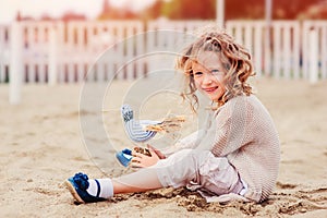 Happy child girl playing with toy bird on the beach
