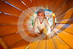 Happy child girl playing in tunnel on playground
