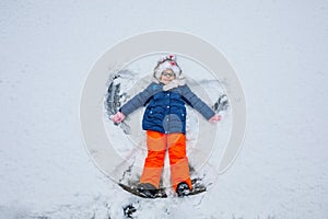 Happy child girl playing on a winter walk in nature. Kid making snow angel. Happy preschool girl having fun on snowing