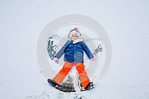 Happy child girl playing on a winter walk in nature. Kid making snow angel. Happy preschool girl having fun on snowing