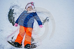 Happy child girl playing on a winter walk in nature. Kid making snow angel. Happy preschool girl having fun on snowing