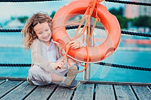 Happy child girl plays with rescue ring on wooden pier with sea background