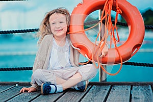 Happy child girl plays with rescue ring on wooden pier with sea background