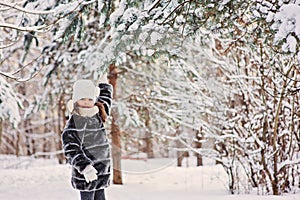 Happy child girl plays with snow on pine tree in winter forest